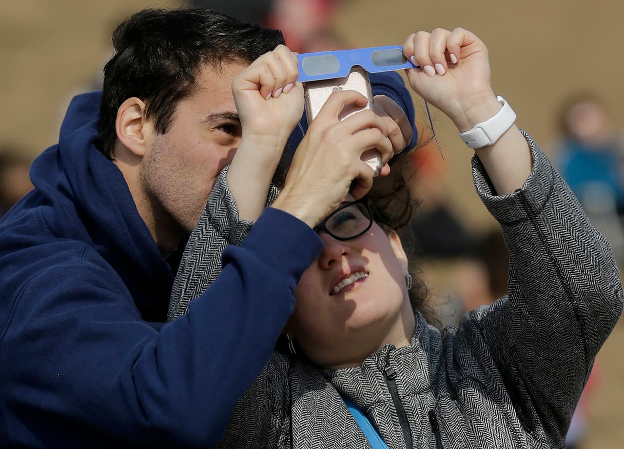 Liza Leykina sostiene un par de gafas para que Mark Solovey tome una foto del eclipse solar a través de su celular en Bernal Heights Hill, San Francisco.