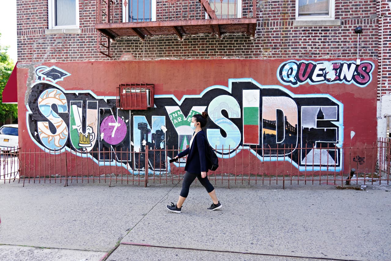 Una mujer con mascarilla pasea delante de un mural en Sunnyside, en Queens, en la ciudad de Nueva York.