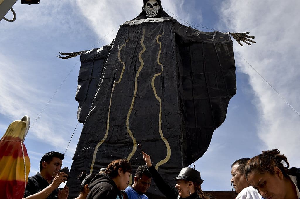 Además de la influencia azteca, está también la de los mayas, quienes rendían tributo a Ah Puch, o Ah Cimih, el dios y rey de Mtnal, el inframundo. Ellos lo representaban como un esqueleto o cadáver con un rostro de jaguar (o a veces búho) adornado con campanas.