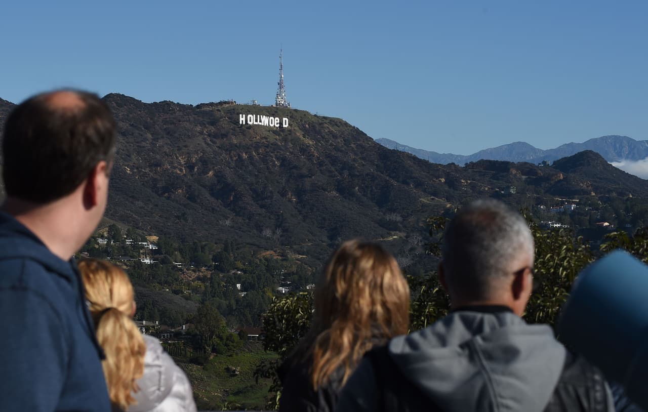 Tourists visiting the Hollywood Bowl Overlook see the Hollywood sign reading "Hollywoed" before repair crews completed their work to return the sign to its normal state, after vandals converted it to read "Hollyweed," January 1, 2017 in Hollywood, California. Police said unidentified thrill-seekers had climbed up and arranged tarps over the two letter "O's" to make them look like "E's," CBS affiliate KCAL reported. Each letter is 45 feet (13.7 meters) high, so the feat would have required not just bravado but considerable athleticism. / AFP / Robyn Beck (Photo credit should read ROBYN BECK/AFP/Getty Images)