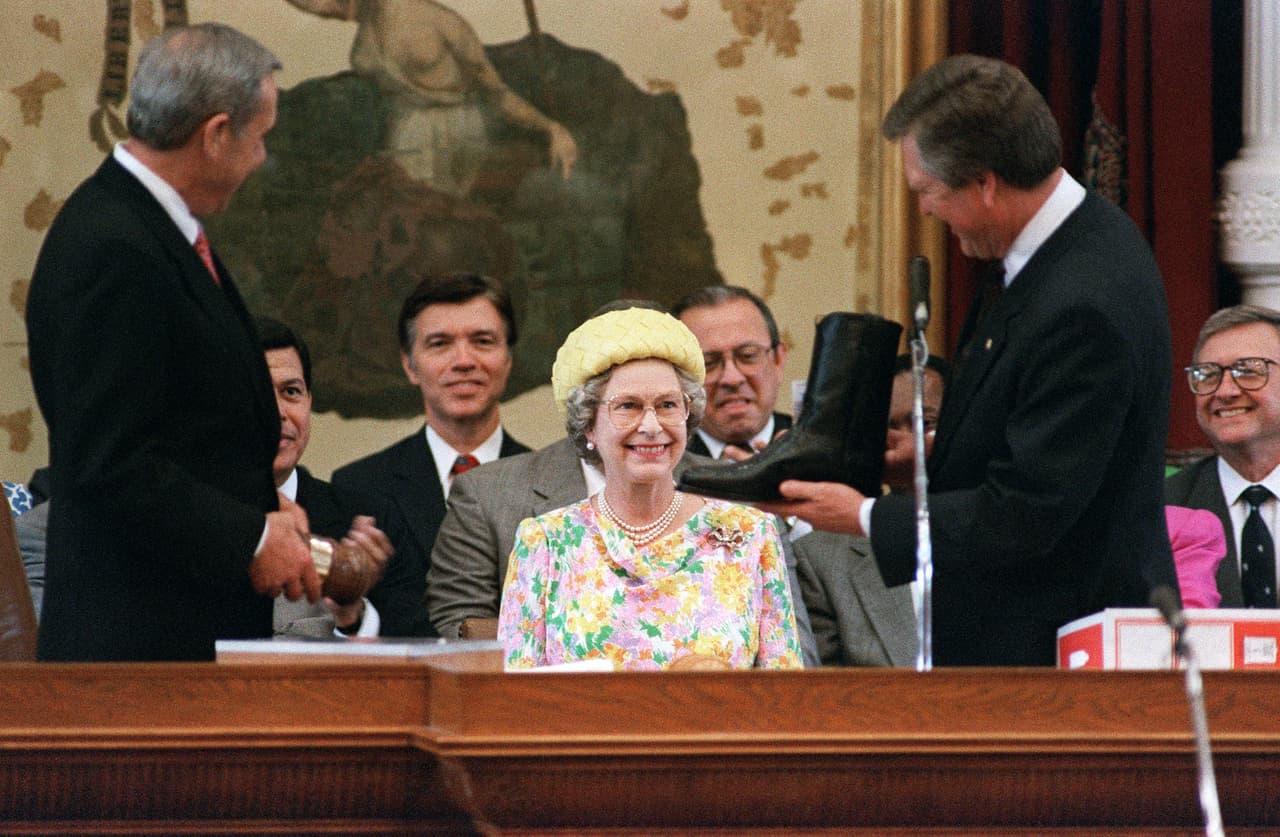 Queen Elizabeth II smiles as she is displayed a pair of boots by Texas Speaker of the House Gib Lewis, in Austin 20 May 1991. The Queen is on a three-day visit of Texas during her tour of the United States. (Photo by CHRIS WILKINS / AFP) (Photo by CHRIS WILKINS/AFP via Getty Images)