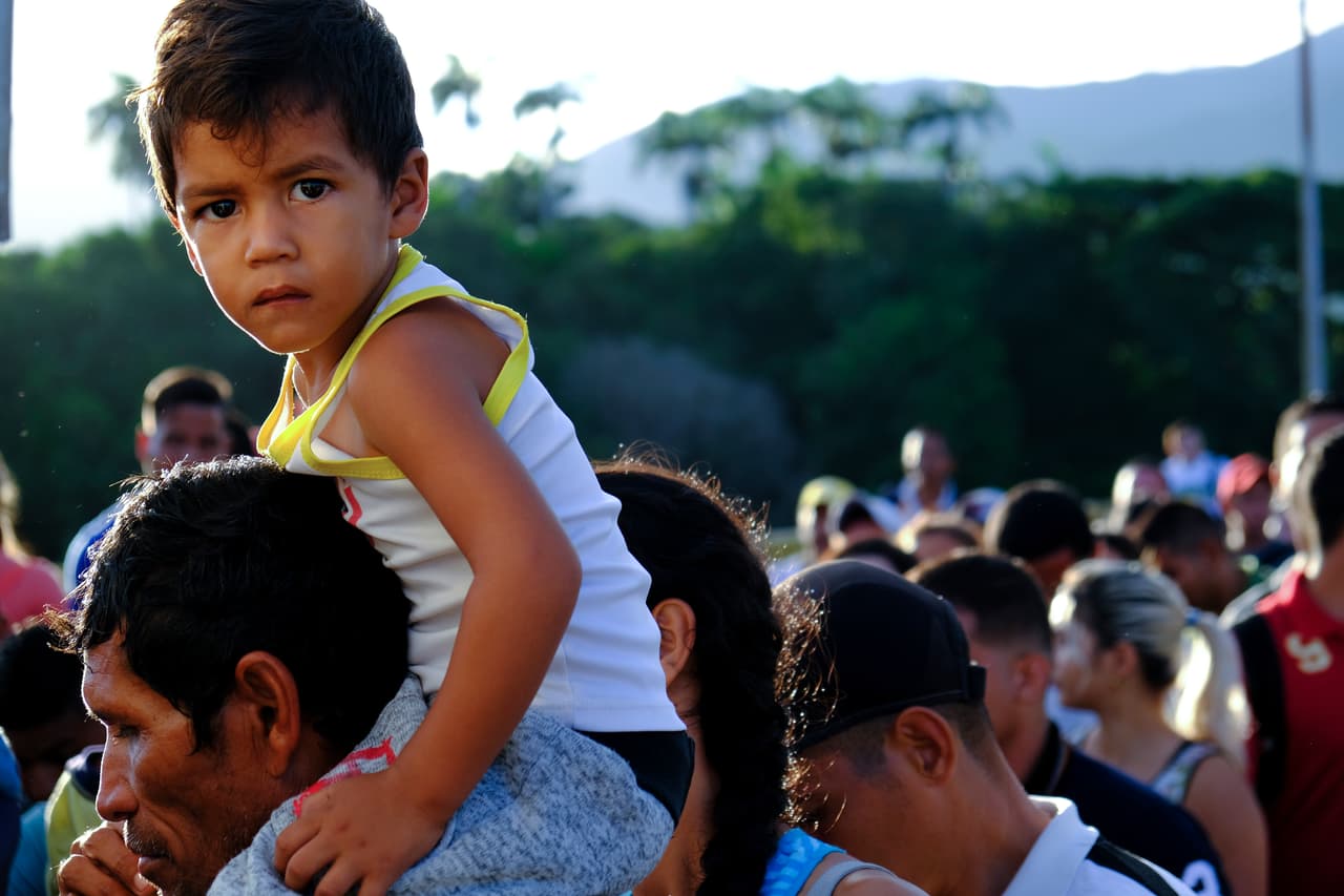 Un venezolano con un niño sobre los hombros espera para cruzar el puente internacional Simón Bolívar a Cúcuta, Colombia, el sábado 8 de junio de 2019.