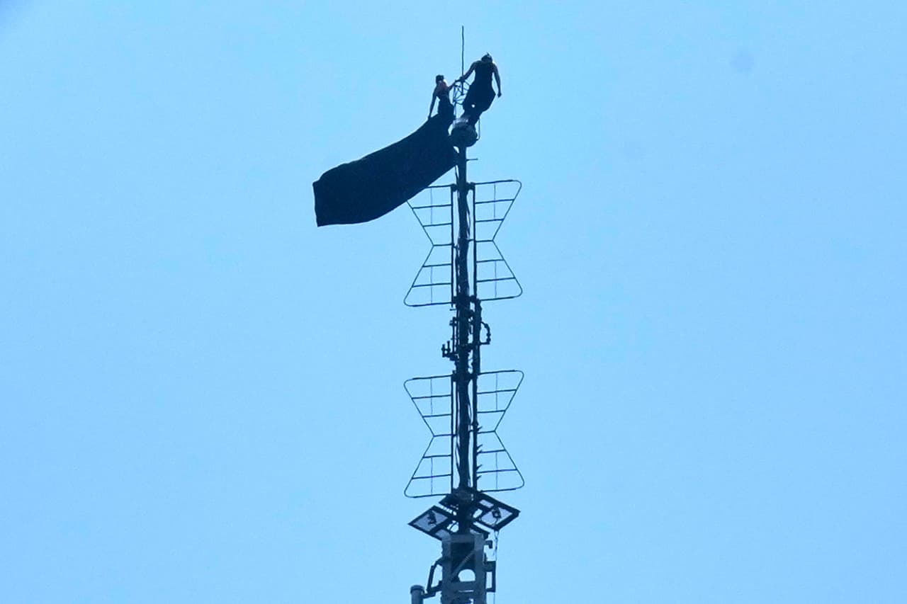 Two people stand on the tip of the antenna of the Empire State Building while holding a banner on Wednesday, July 1, 2026. (AP Photo/Richard Drew)