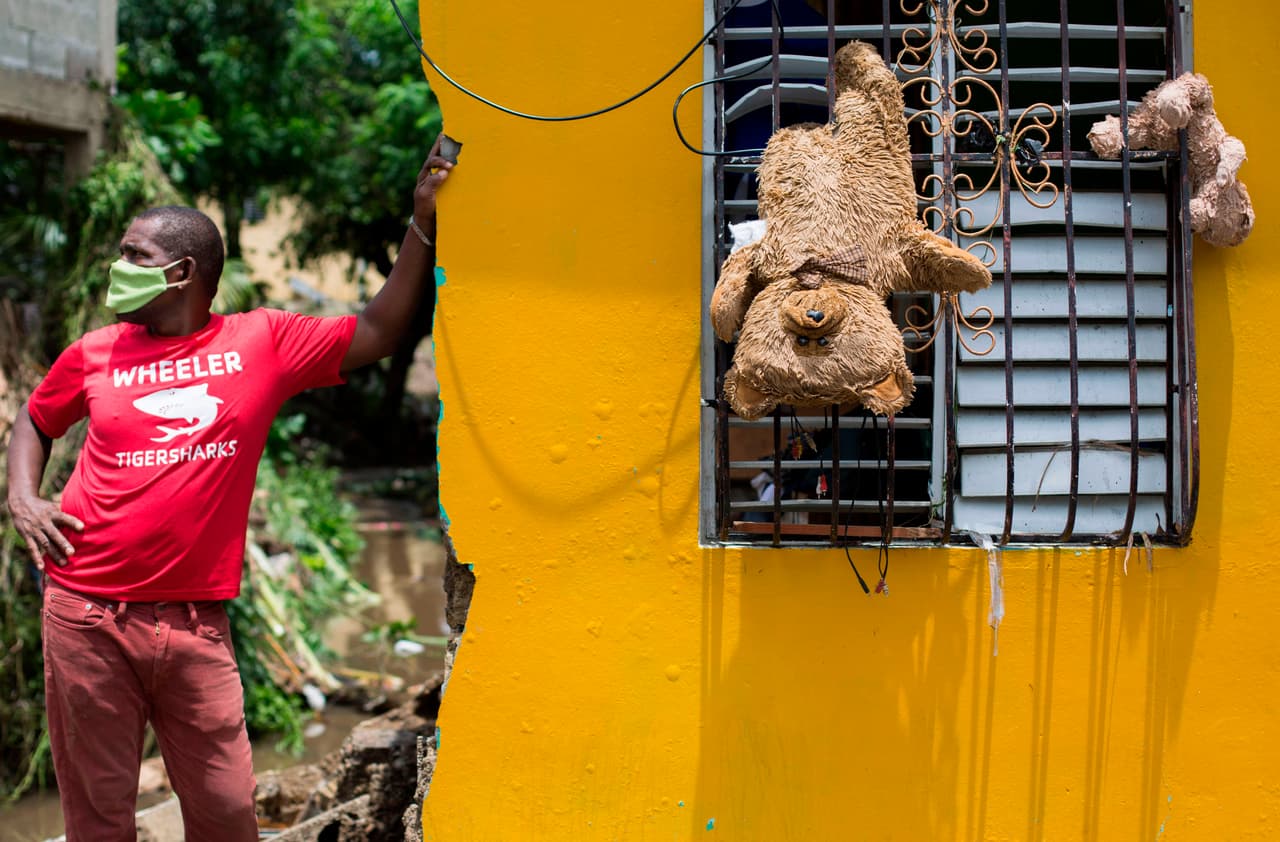 Un hombre afuera de su casa, donde los osos de peluche fueron colgados de una ventana para que se secaran después del paso de la tormenta tropical Isaías.