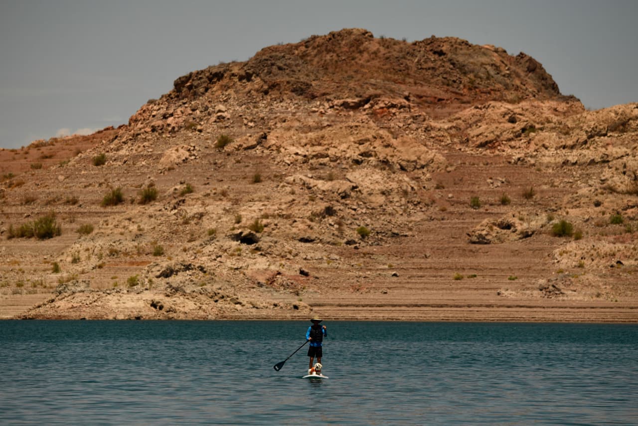 Un surfista de remo monta con un perro con los niveles bajos de agua debido a la sequía occidental el 20 de julio de 2021 en el puerto deportivo del lago Mead en el río Colorado en Boulder City, Nevada. - El embalse del lago Mead formado por la presa Hoover en la frontera entre Nevada y Arizona proporciona agua al suroeste, incluidas las ciudades de Las Vegas, así como poblaciones en Arizona y California.