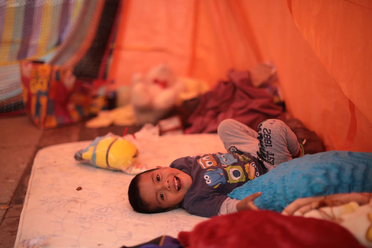 La inocencia de un pequeño, que tuvo que ser evacuado junto a su familia de su casa en peligro de derrumbe, muestra un gesto de alegría al tener que dormir en una tienda fuera de casa.