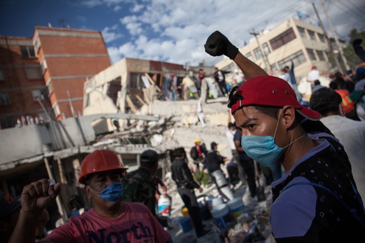 Rescuers and volunteers raise their fists high in order to keep silence around ruined buildings. At least two schools were collapsed by the magnitude 7.1 earthquake.