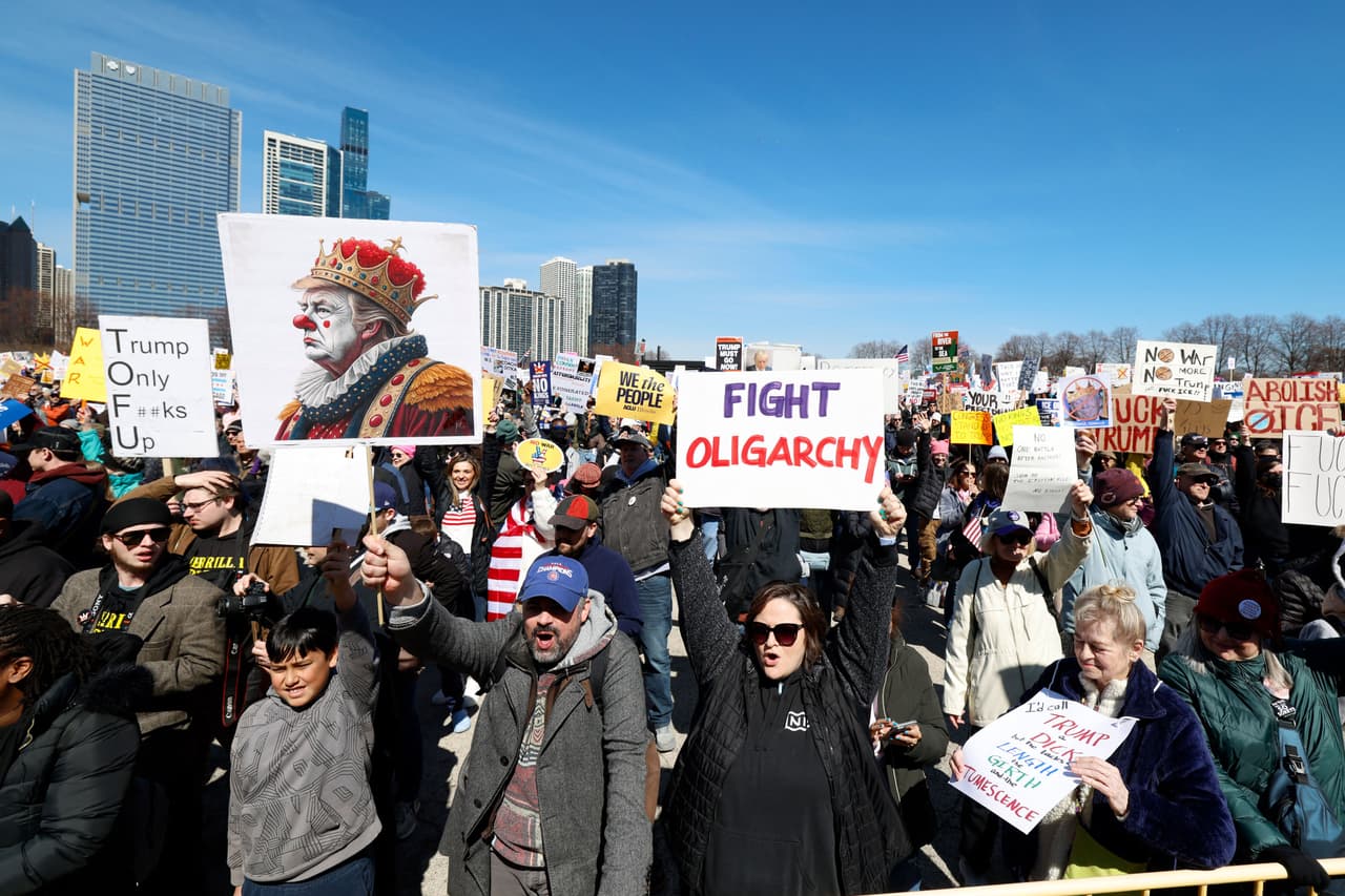 Una persona sostiene un cartel con una imagen del presidente de Estados Unidos, Donald Trump, con maquillaje de payaso, en una clara señal de burla e ironía durante la protesta.