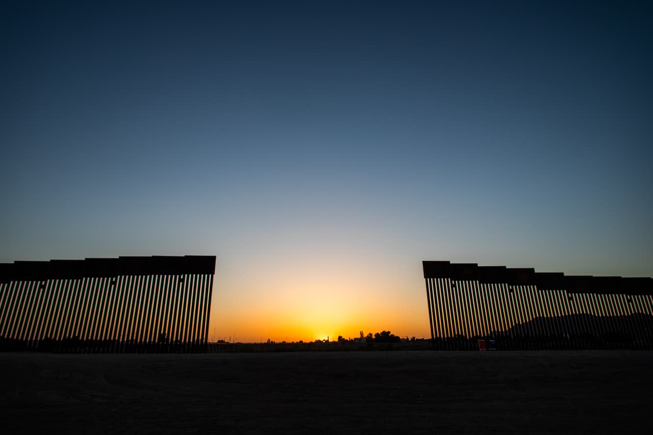 El sol se pone en el lado mexicano de la frontera entre Estados Unidos y México detrás de una abertura en el muro fronterizo en Yuma, Arizona por donde están cruzando cientos de mexicanos, centro y suramericanos. La administración Biden está tratando de desarrollar un plan para manejar de manera segura el aumento de inmigrantes que cruzan la frontera sur.
