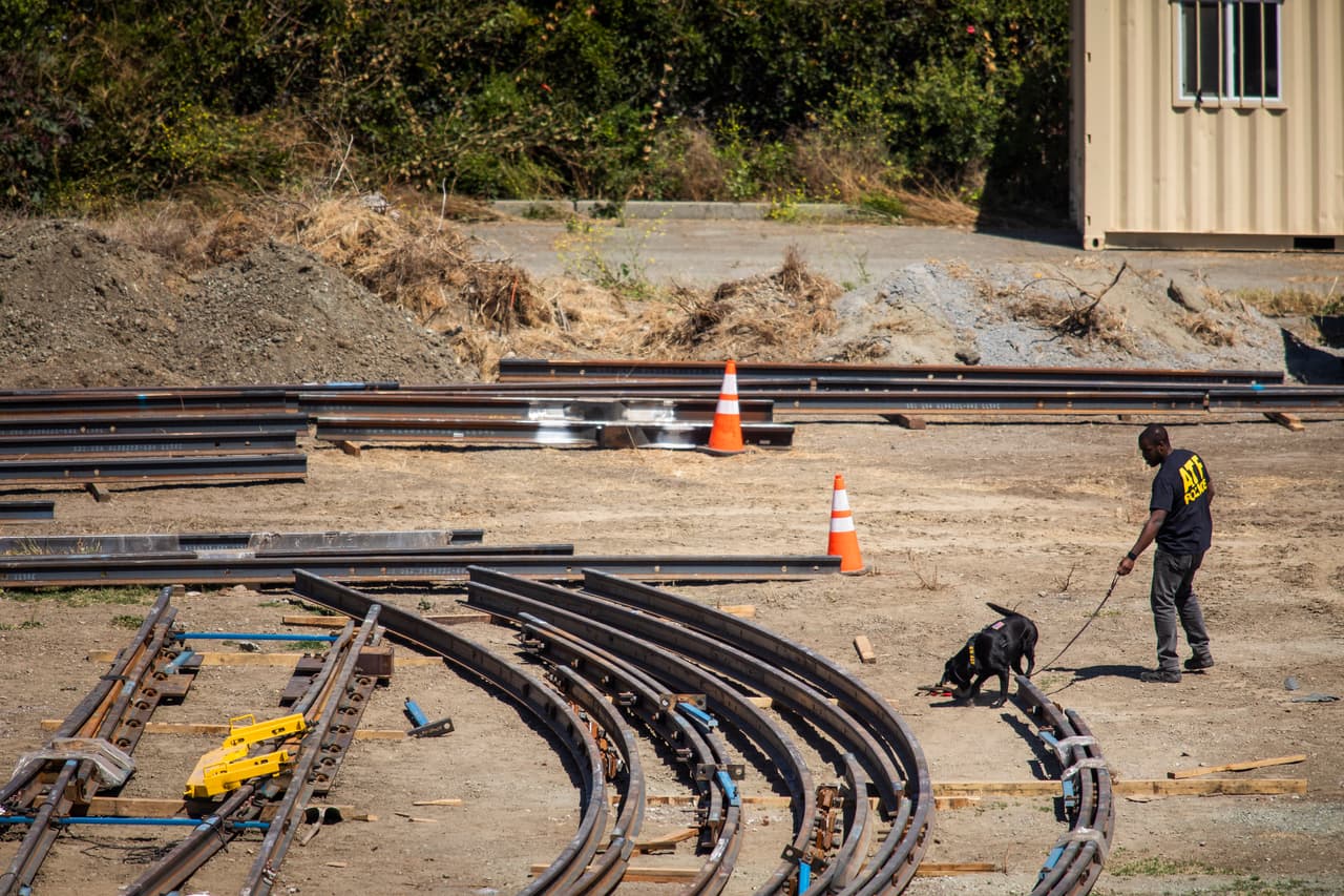 Un agente de la Agencia para el Control de Armas revisa la zona del tiroteo en las instalaciones del VTA con la ayuda de un perro entrenado para detectar explosivos.