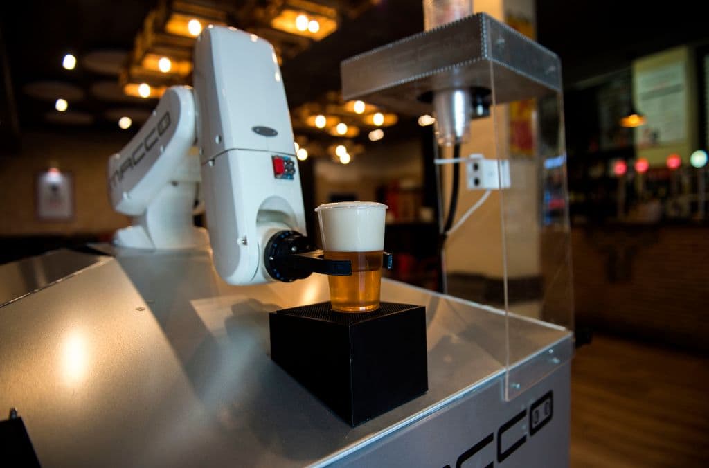 Ubicada en la entrada del bar, la máquina consiste en un grueso brazo articulado de color blanco con una pinza en el extremo que sujeta los vasos de plástico.