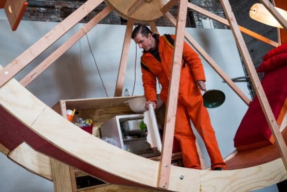 Hay veces que la monotonía de la vida se siente como una rueda de hámster gigante. De eso se trata el último performance de los artistas Ward Shelley y Alex Schweder de Brooklyn, quienes crearon una rueda de hámster de tres pisos en la que tendrán que coordinar cada movimiento durante 10 días. El performance llamado "En "rbita", está ubicado en una antigua sala de calderas en Williamsburg. Durante el performance, Schweder y Shelley van a comer, dormir, trabajar, ir al baño, etc, sin bajar de la rueda.