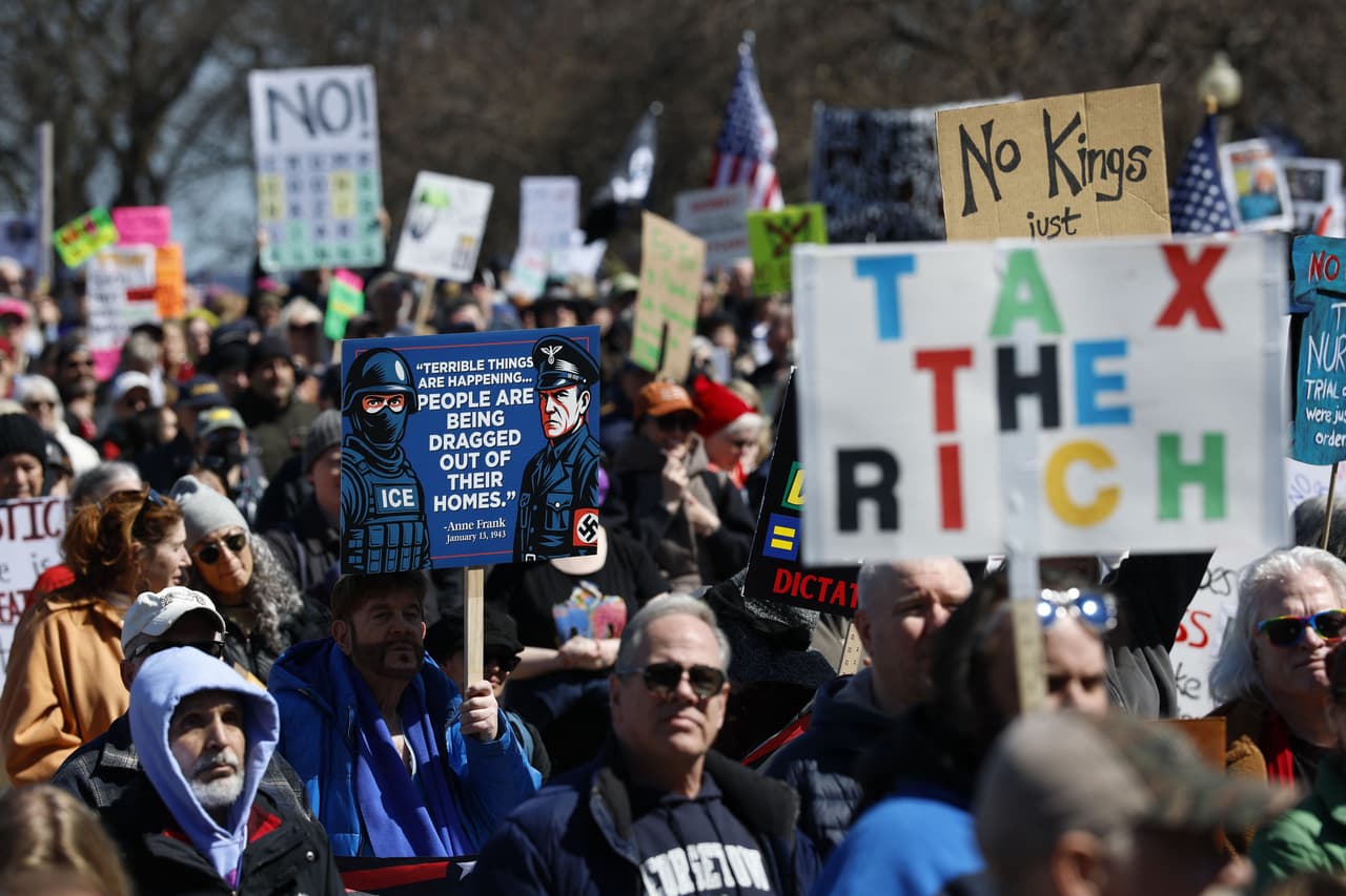 Una persona sostiene un cartel con una cita de Anne Frank, acompañado de imágenes de un agente de ICE y un soldado de la Alemania nazi, mientras participa en una manifestación en Grant Park. La cita en el cartel dice: “Están ocurriendo cosas terribles… las personas están siendo sacadas de sus hogares”.