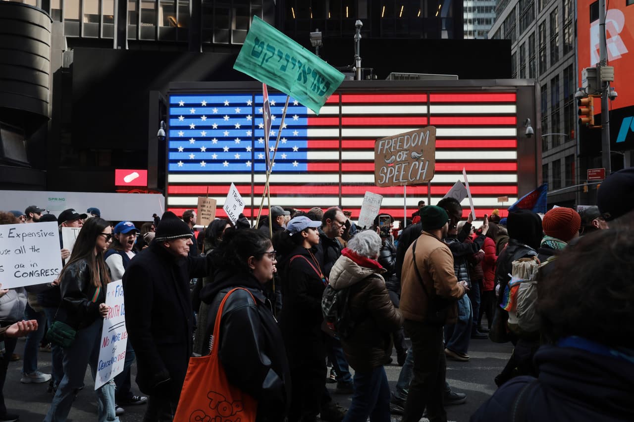Frente a una bandera de Estados Unidos, los participantes exigen libertad de expresión durante la tercera marcha No Kings.