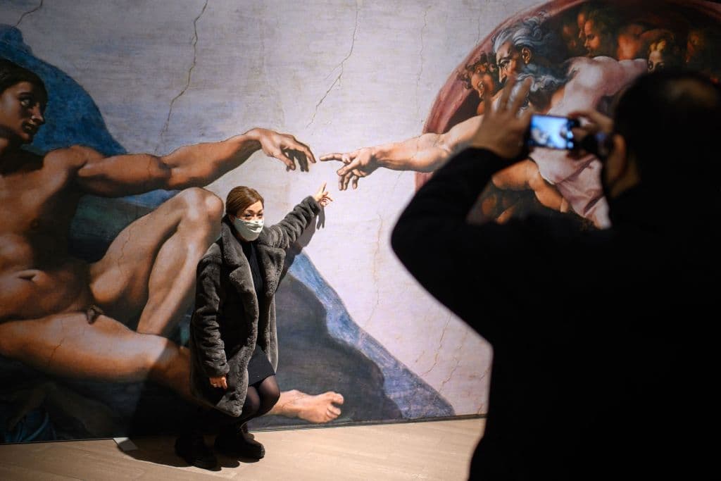 Un visitante posa para una fotografía delante de «La Creación de Adán» mientras asiste a la exposición «La Capilla Sixtina de Miguel Ángel» en el Trafford Palazzo de Manchester, al noroeste de Inglaterra, el 11 de febrero de 2022. - La exposición reproduce 34 de los frescos del techo de Miguel Ángel de la Capilla Sixtina del Vaticano, que se muestran en su tamaño original. (Foto de OLI SCARFF/AFP vía Getty Images)
