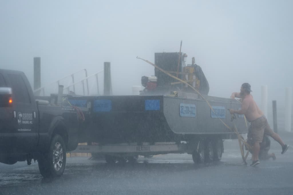 Un hombre lucha por asegurar el equipo de construcción contra el oleaje, empujado por los vientos de la tormenta tropical Debby, en Cedar Key, Florida, el domingo 4 de agosto de 2024.