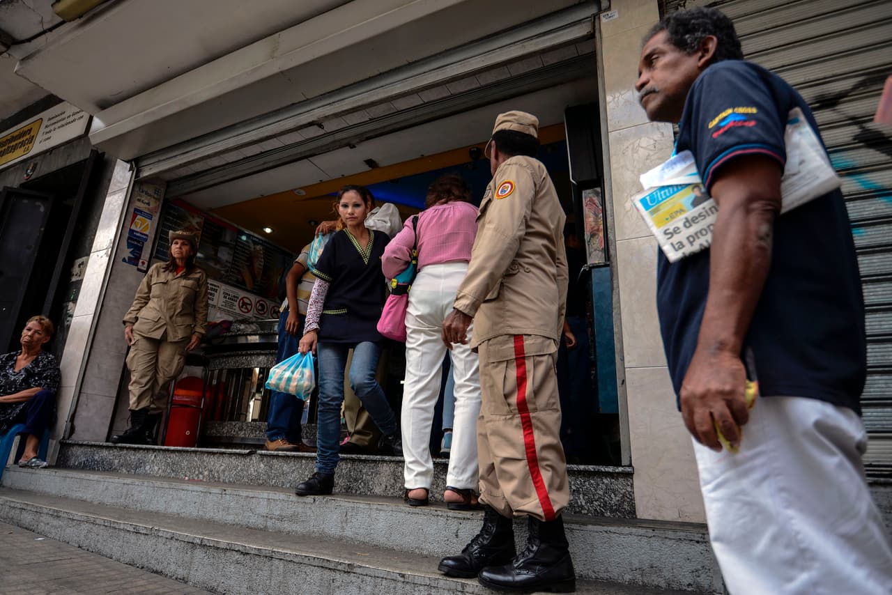 Una pareja de milicianos vigila la fila de gente formada para comprar pan en uno de los comercios expropiados.