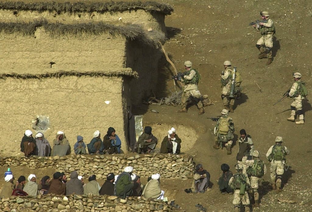 Aldeanos afganos observan a los soldados estadounidenses registrando una casa en busca de talibanes y fuerzas de Al Qaeda. Era una de las etapas finales de la "Operación Viper" en la provincia de Helmand, en el sur de Afganistán, en febrero de 2003.
<br>
<br>Aunque en mayo de 2003 el secretario de Defensa, Donald Rumsfeld, había anunciado el fin de las principales operaciones militares estadounidenses en Afganistán, los combates seguían y la amenaza 
<a href="https://www.univision.com/temas/taliban"><u>Talibán</u></a> parecía perpetuarse. Entonces Estados Unidos decidió seguir trasladando recursos militares a ese país.
<br>