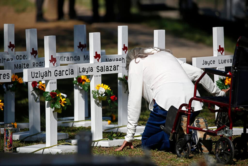 Una mujer se arrodilla mientras presenta sus respetos frente a cruces con los nombres de los niños asesinados afuera de la Escuela Primaria Robb en Uvalde.