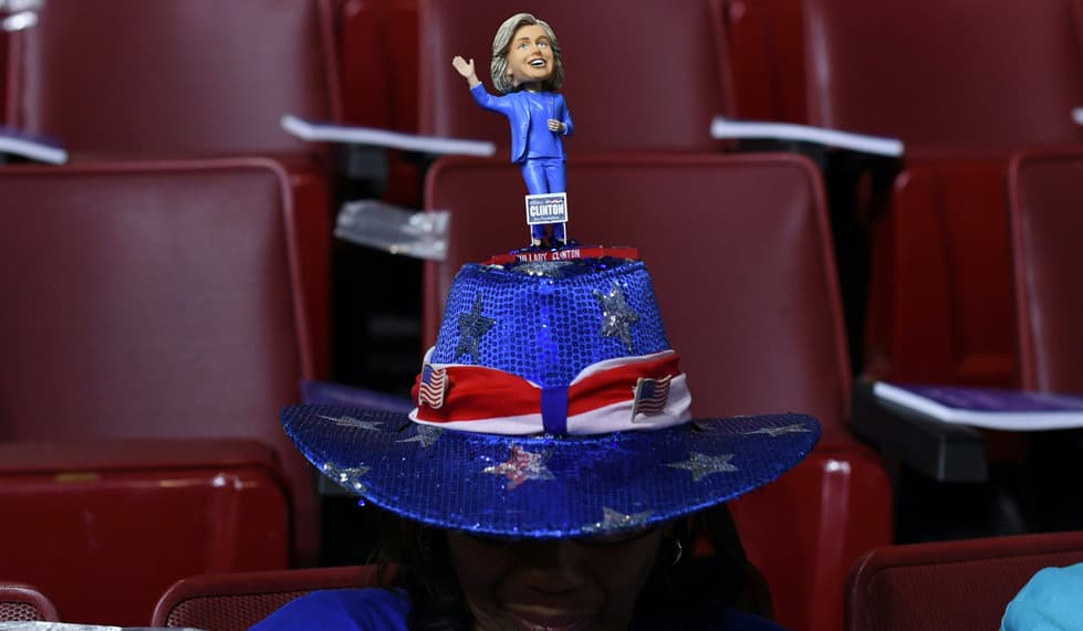 La joya de este sombrero azul con banda bicolor, roja y blanca, estrellas y banderas de Estados Unidos es la versión miniatura de Hillary Clinton. La figura saluda felizmente desde la copa del sombrero estilo vaquero.