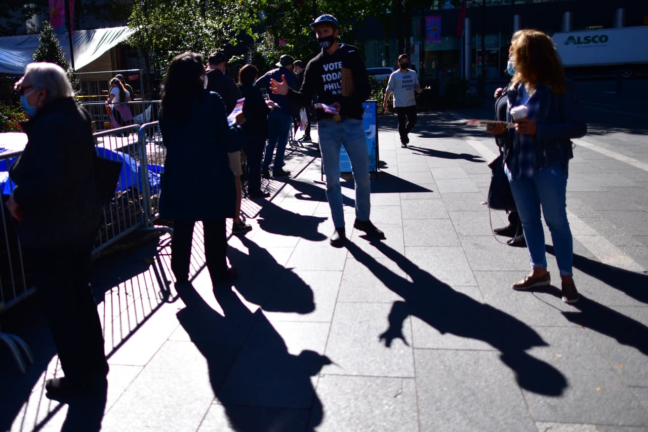 Un voluntario ayuda a los votantes que esperan en fila fuera del Ayuntamiento de Filadelfia a emitir sus boletas de votación.