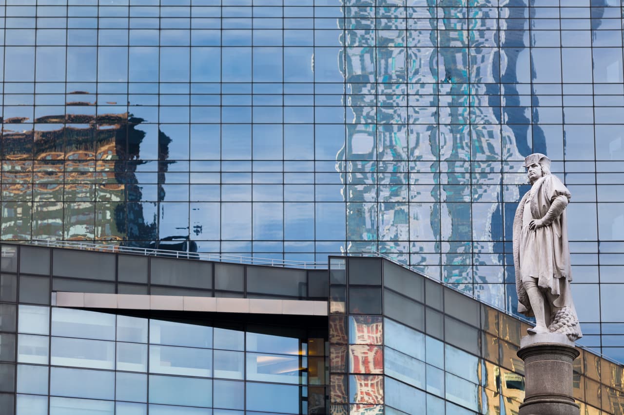 El reflejo de edificios en la fachada del Time Warner Center, en primer plano la estatua de Cristobal Colón.
