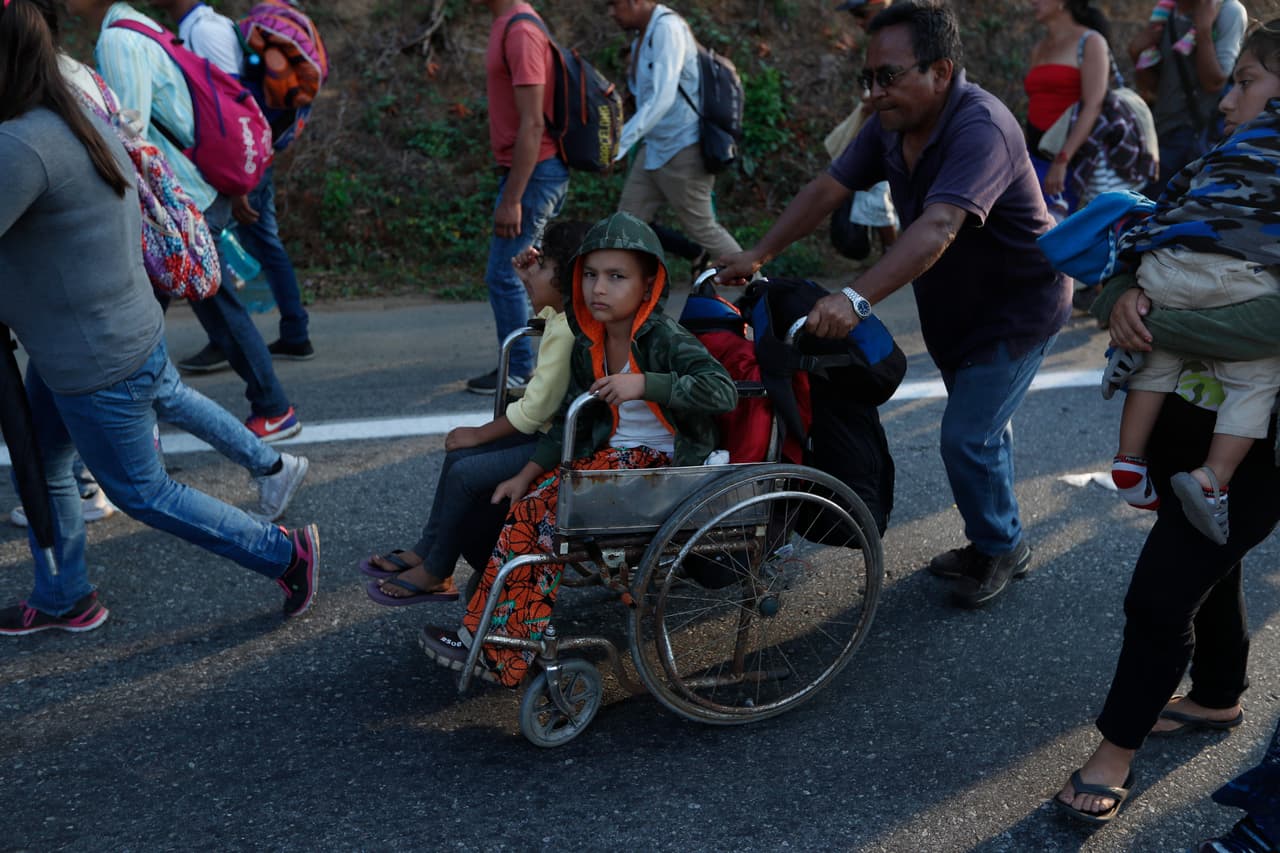 Un migrante, parte de una caravana que se dirige a la frontera entre México y Estados Unidos, empuja la silla de ruedas de un menor por la carretera en Escuintla, Chiapas, México, el sábado 20 de abril de 2019.