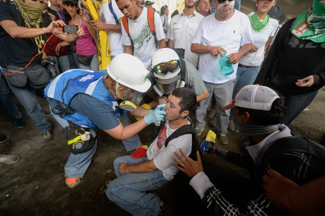 Un manifestante opositor recibe ayuda de paramédicos tras asfixiarse con los gases lacrimógenos durante la manifestación.