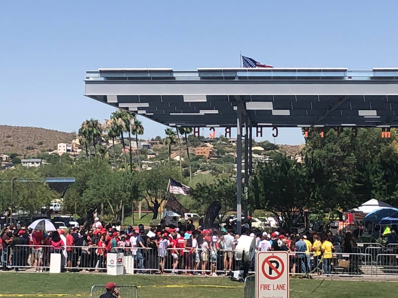 Con sombrillas y gorras, decenas de personas intentan cubrirse del sol y el intenso calor de Phoenix que hoy supera los 100 grados F.