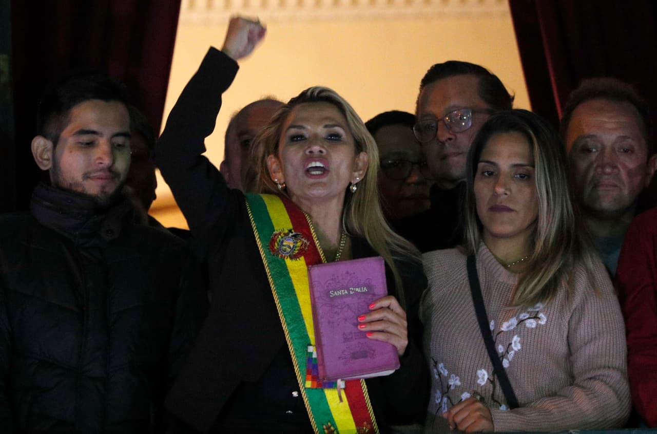La segunda vicepresidenta del Senado, la opositora Jeanine Áñez, al centro, luce la banda presidencial y exhibe una Biblia, mientras pronuncia un discurso ante una multitud desde el balcón del palacio Quemado en La Paz, Bolivia, después de que se autoproclamara presidenta interina del país el martes 12 de noviembre de 2019. (AP Foto/Juan Karita)