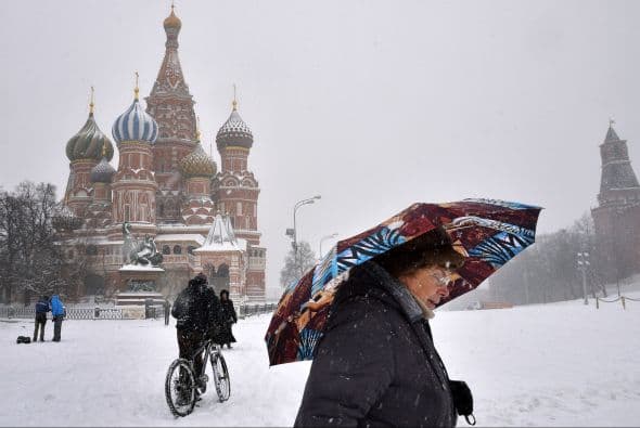 Una mujer camina con un paraguas bajo la nieve frente a la Catedral de San Basilio, en la Plaza Roja de Moscú.