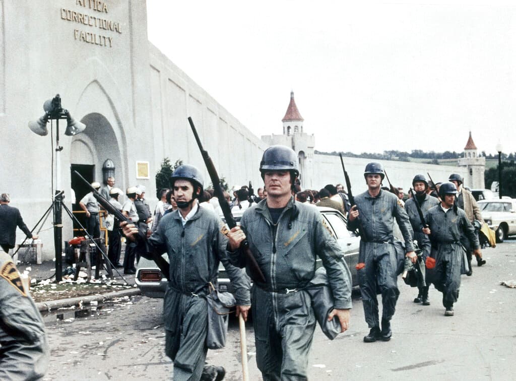 In this Sept. 1971 file photo, armed officers walk by the entrance to the Attica Correctional Facility, in Attica, NY, in the aftermath of the riot at the prison, that left 43 dead over a period of four days. Fifty years after the Attica prison uprising, the families of slain and injured prison guards say they're still waiting for an apology from the state.