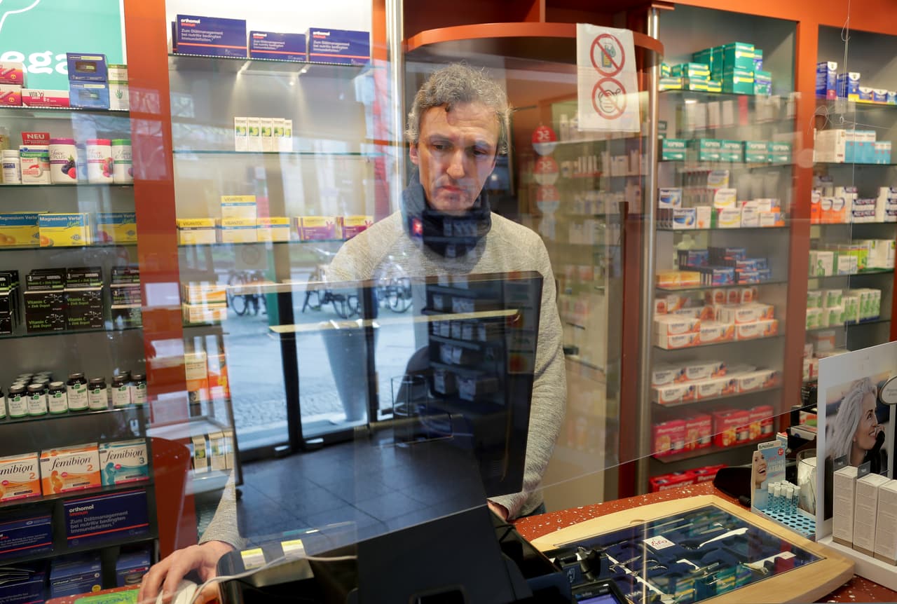 El propietario de una farmacia de Berlín, Alemania, detrás de la barrera acrílica que instaló para atender a sus clientes con seguridad. 19 de marzo
