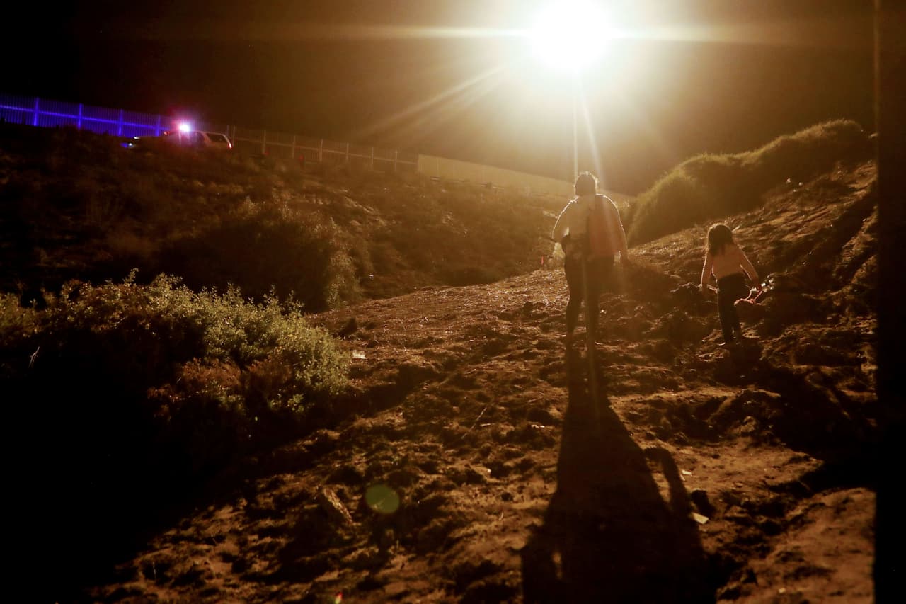 Una migrante y una niña después pasar la valla sur. Al fondo un auto de la Patrulla Fronteriza.
