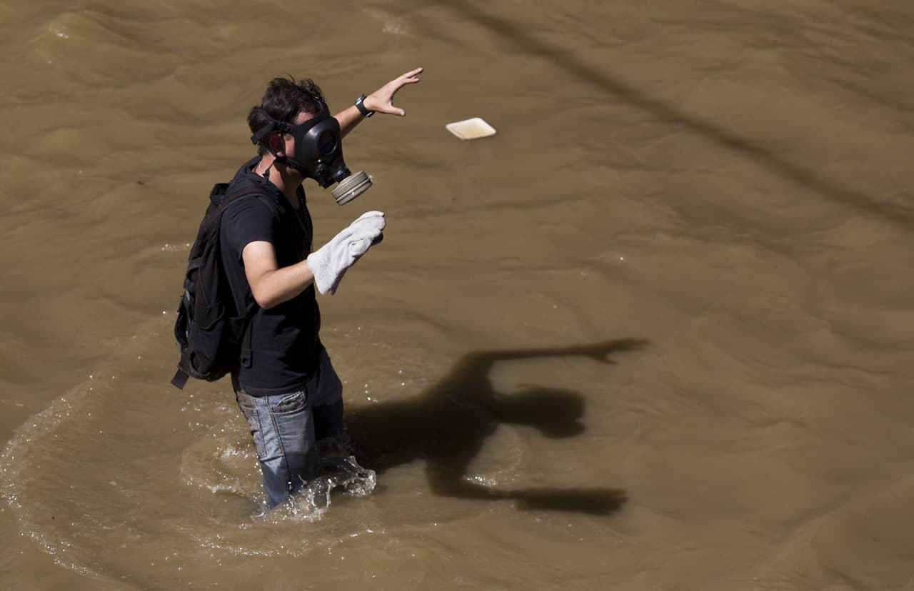 A protester with a gas mask crosses the Guaire river. The gas mask serves to protect wearers from tear gas as well as the stench of sewage in the river.