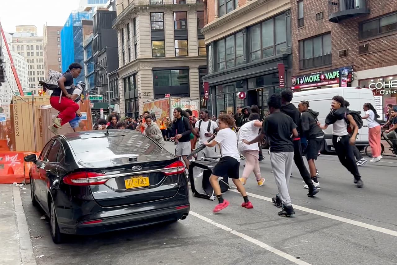 Un hombre salta sobre un automóvil mientras una multitud corre por la calle en Broadway cerca de Union Square.