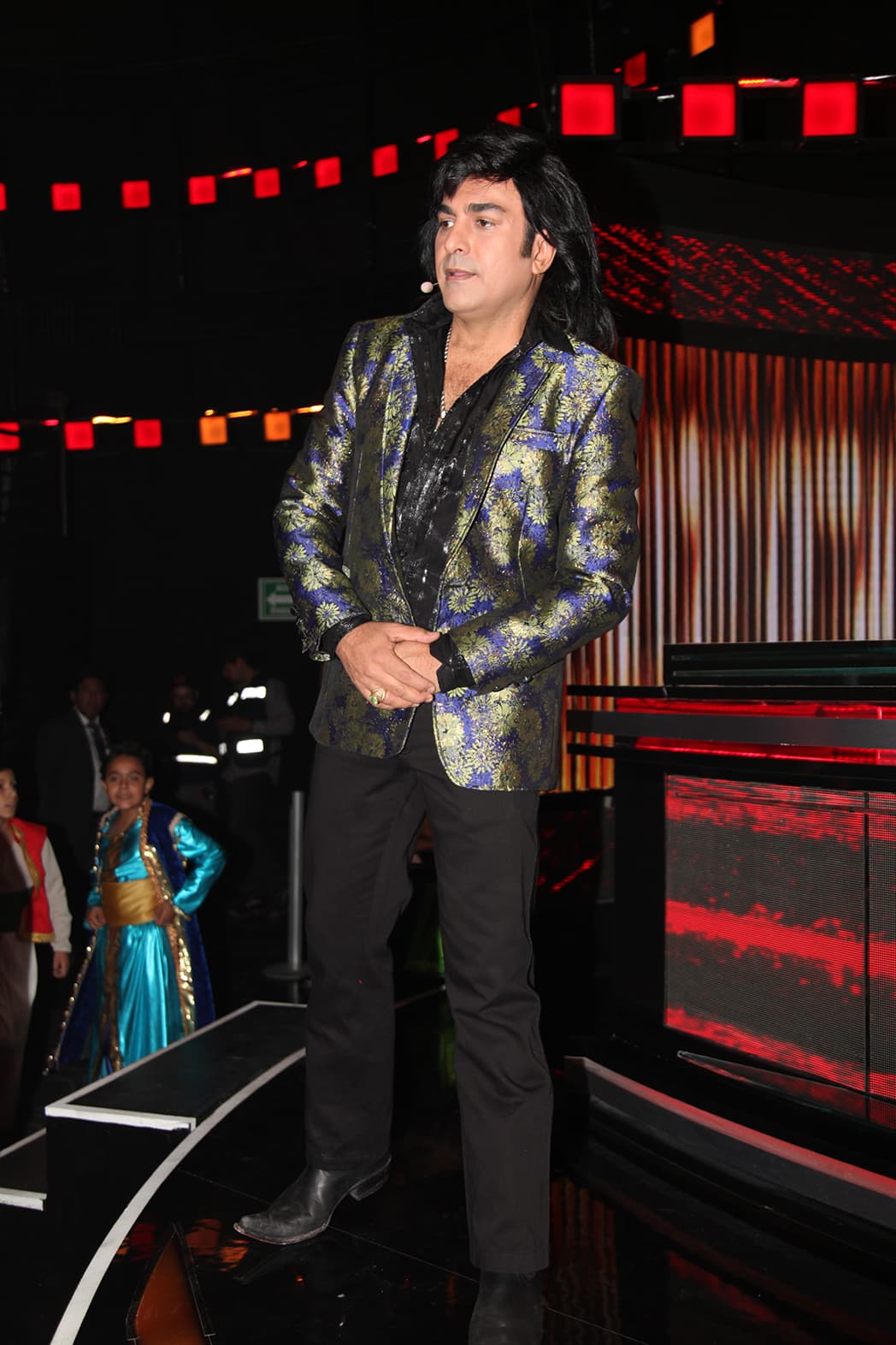 El saco floreado era color verde y azul, lo combinó con un pantalón y camisa negra, así como botas puntiagudas en el mismo tono.