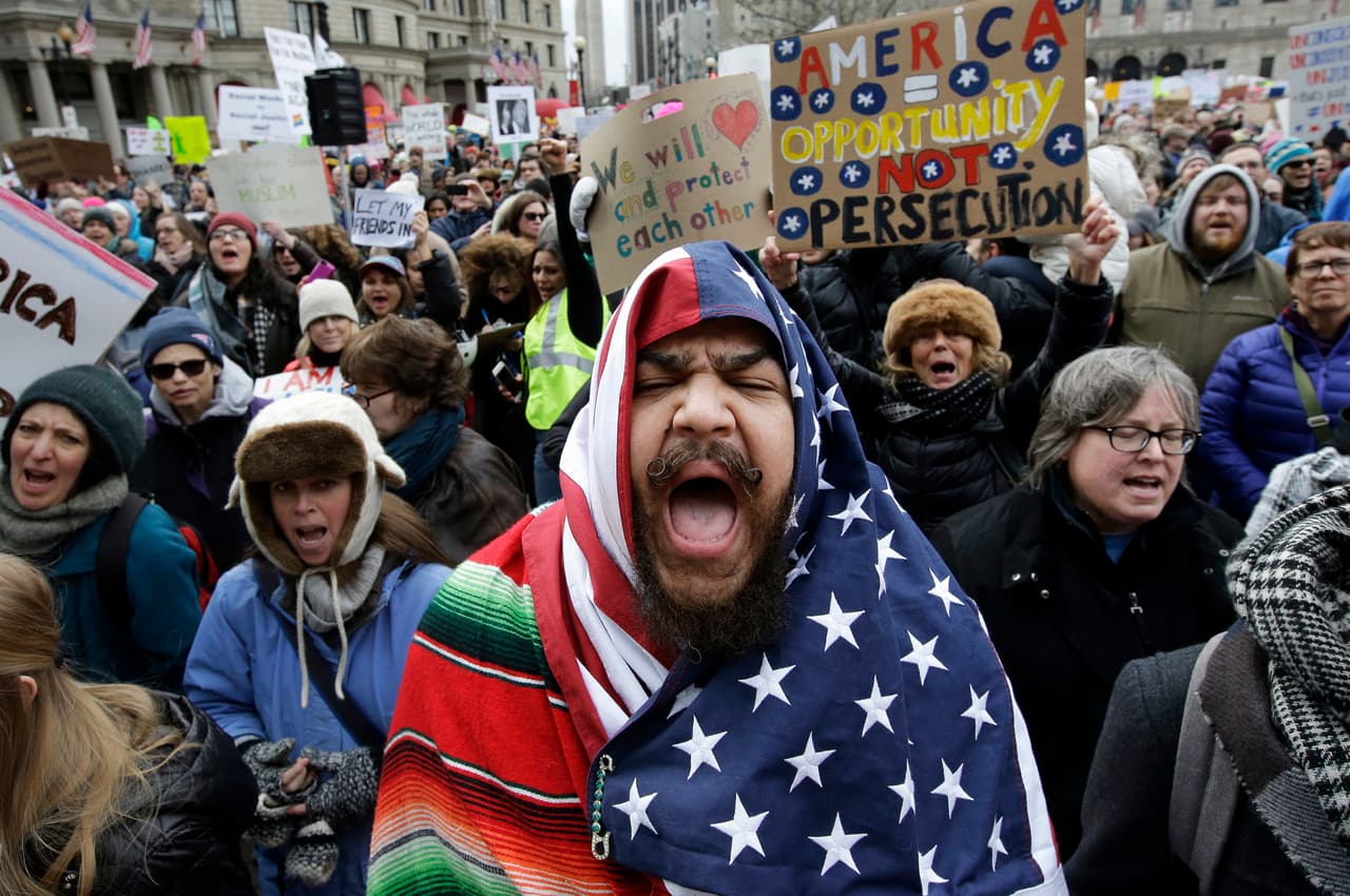 Un hombre posa con una bandera estadounidense delante de un cartel que dice: "América = Oportunidad, no persecución".