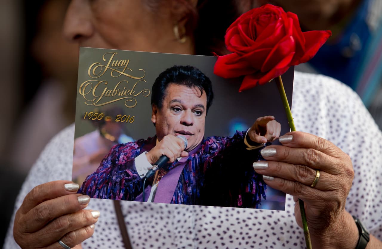 Una mujer sostiene una imagen de Juan Gabriel cerca de una estatua del cantautor mexicano en la plaza Garibaldi, en la Ciudad de México, el martes 30 de agosto del 2016. Juan Gabriel murió el domingo 29 de agosto en su casa en California. Tenía 66 años. Sus restos llegarán a Ciudad Juárez el sábado 3 de septiembre. (AP Foto/Eduardo Verdugo)