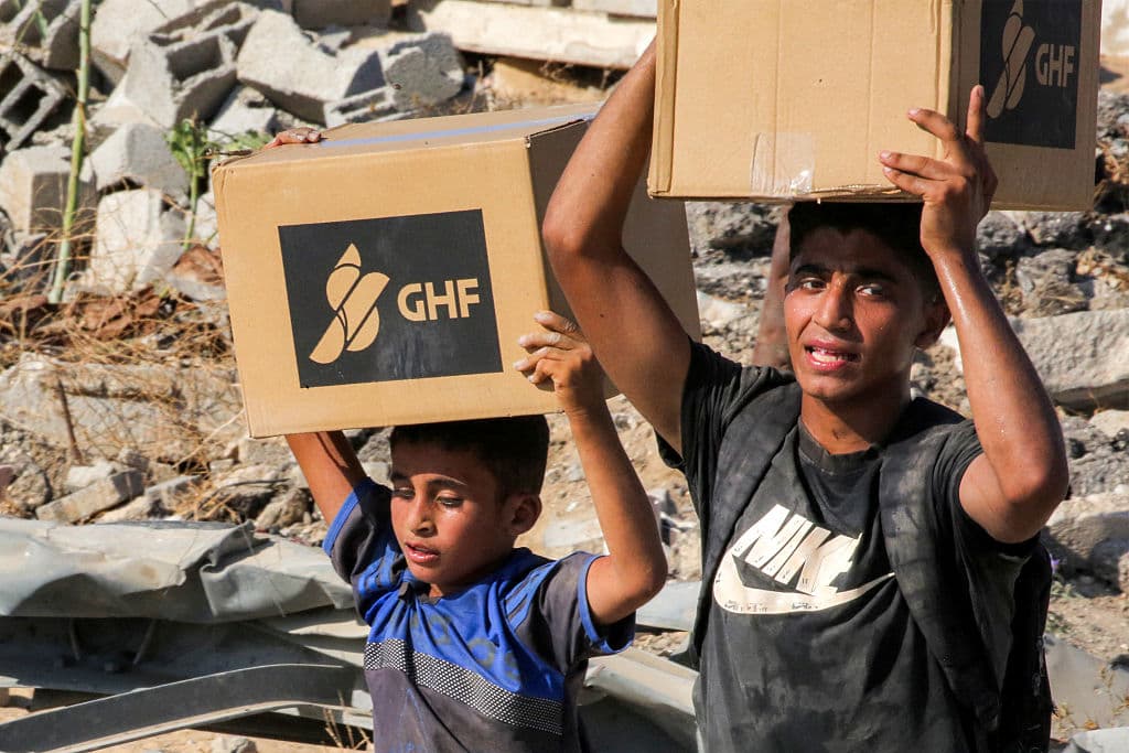 Unos niños caminan con cajas de ayuda humanitaria que han recibido en un centro de distribución gestionado por la Fundación Humanitaria de Gaza (GHF), respaldada por Estados Unidos e Israel, mientras cruzan el llamado "corredor de Netzarim" en el centro de la Franja de Gaza, el 22 de agosto de 2025.