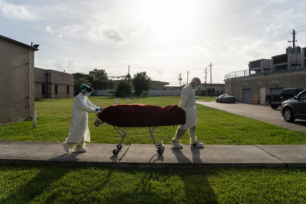 Personal médico con trajes de protección transportan a un fallecido por covid-19 a un vehículo para ser llevado a una morgue.
