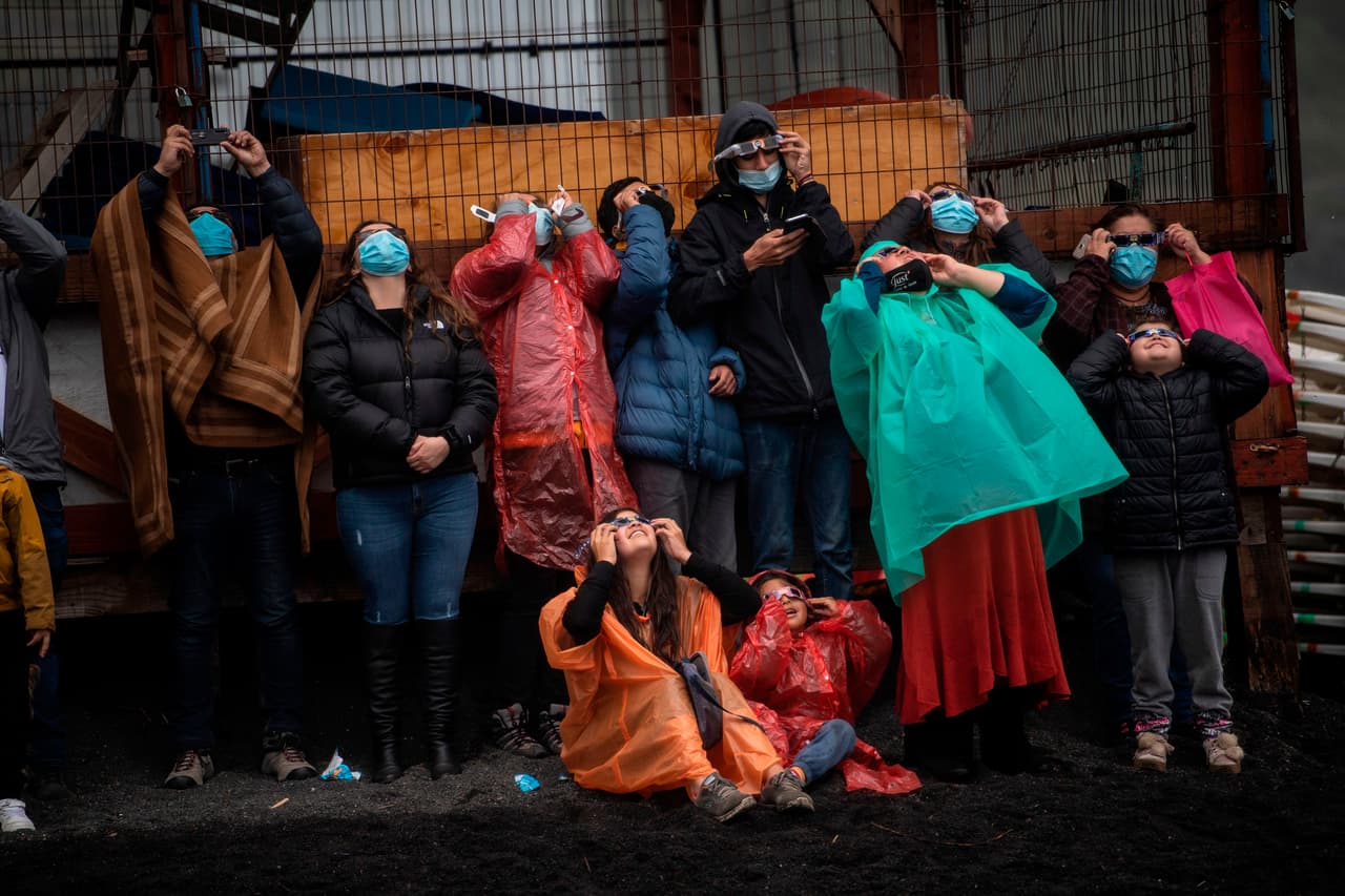 Personas observan el eclipse total de sol en las orillas del lago Villarrica, Chile, utilizando máscaras para evitar la propagación del coronavirus y ropa gruesa para protegerse de la fuerte lluvia que azotó la región horas antes del suceso de este lunes 14 de diciembre.
<br>
<br>Este año el eclipse tiene lugar en plena pandemia del covid-19, que ha dejado en Chile más de 560,000 contagios y que en las últimas semanas ha dado señales de una segunda ola, por lo que las autoridades insistieron en que se cumplieran las restricciones sanitarias y evitaran aglomeraciones durante el evento.