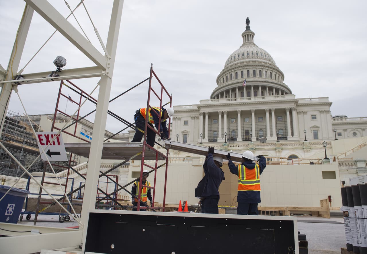 Trabajadores sobre una estructura de andamios que continúa levantada frente al Capitolio, a solo días del evento inaugural.