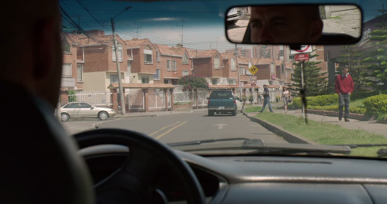 No drug lord can stop looking behind their back, in case someone is watching. Who watches from the car, and who are they watching?