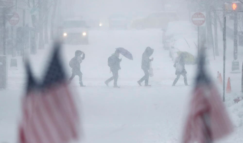 American flags are backdropped by people walking across a snow-covered intersection, Thursday, Feb. 9, 2017, in Hoboken, N.J. A powerful, fast-moving storm swept through the northeastern U.S. Thursday, making for a slippery morning commute and leaving some residents bracing for blizzard conditions. (AP Photo/Julio Cortez)