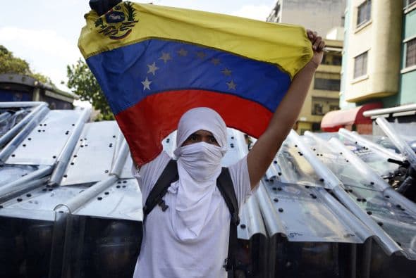 Los estudiantes desarmados portan banderas y gritan consignas contra el gobierno del mandatario Nicolás Maduro. Los estudiantes llevaron a cabo una manifestación pacífica contra el régimen del mandatario Nicolás Maduro el 12 de febrero de 2014. Motorizados uniformados y con sus caras cubiertas, dispararon contra los manifestantes, matando a dos estudiantes y a un oficial.