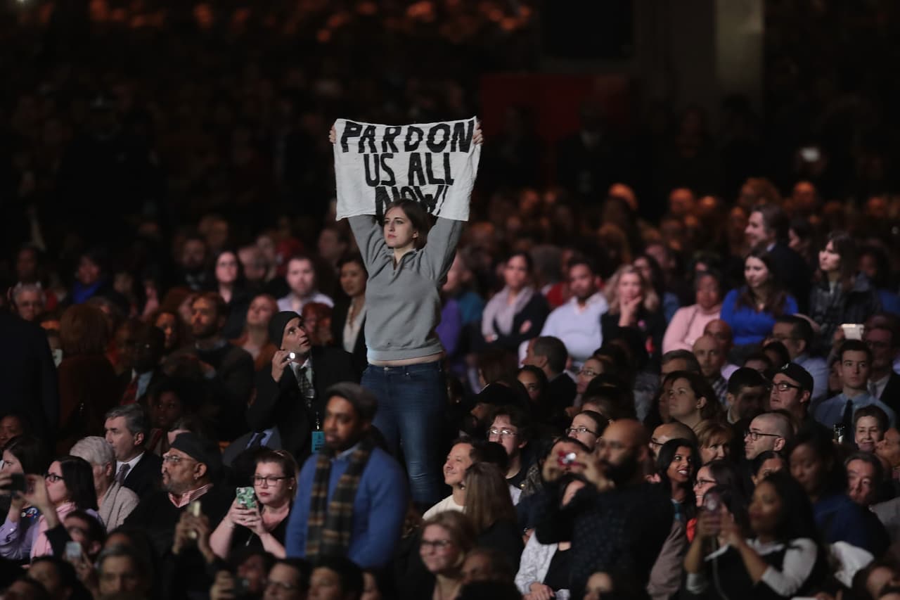 Un asistente muestra un cartel que tiene escrito en inglés “perdónanos ahora” durante el último discurso del presidente.