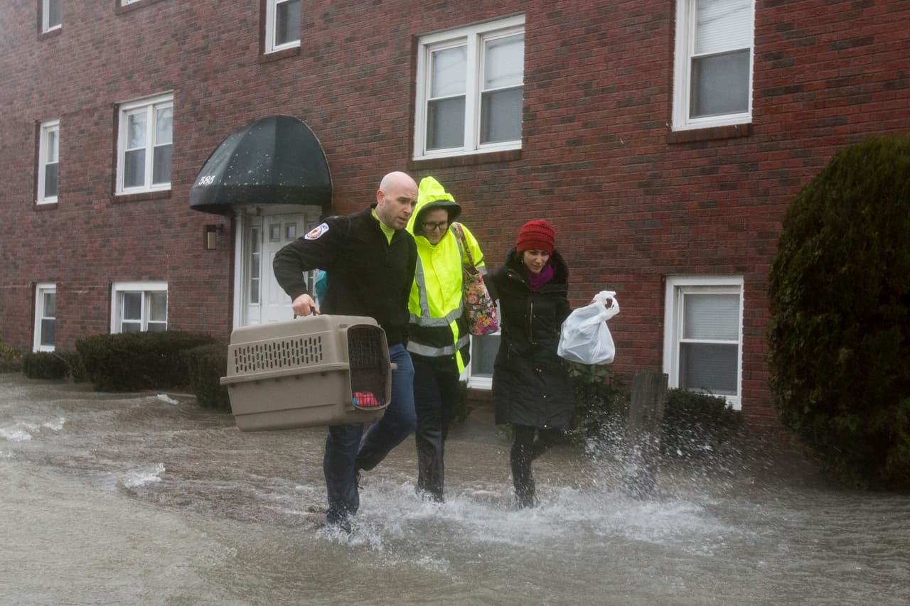 Un trabajador de emergencias carga con un animal de compañía rescatado junto a los vecinos de un bloque de apartamentos inundado en Quincy, Massachusetts.