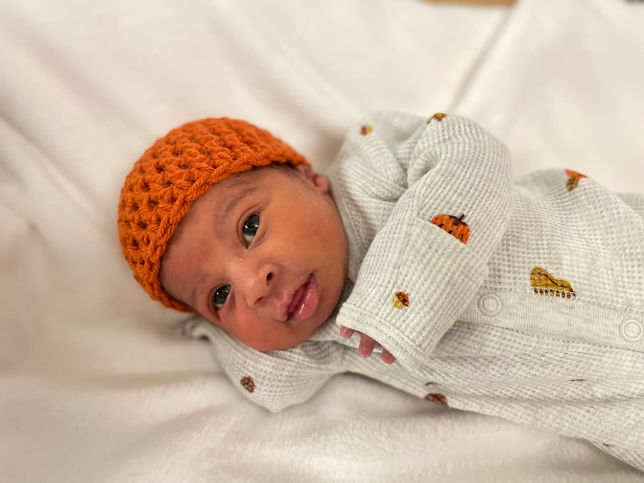 Este bebé tiene un lindo gorrito naranja y un traje de calabazas para esperar su primer Día de Acción de Gracias.