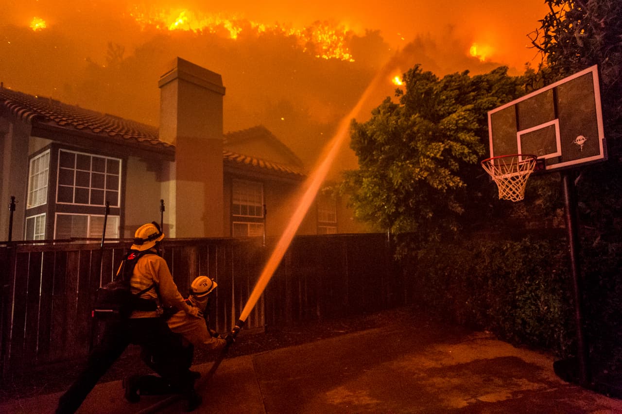 Bomberos intentan salvar las viviendas de un barrio en la cuadra 4,200 de San Ramon Drive, en la ciudad de Corona.